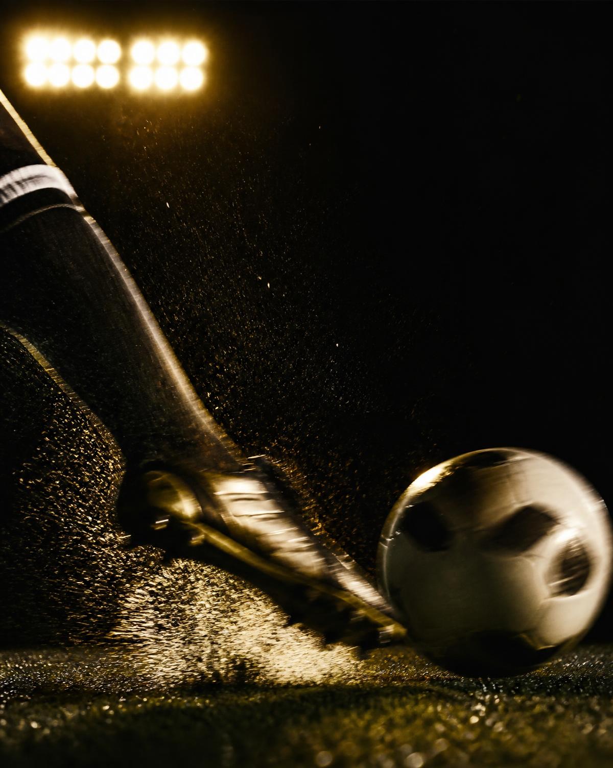 A football struck by a boot in motion under stadium floodlights